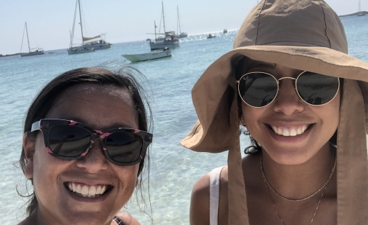 Two women smiling by the ocean with sailboats behind them