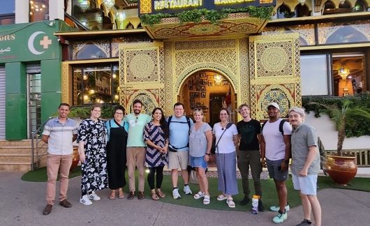 Group photo of adults posing in front of a colorful building