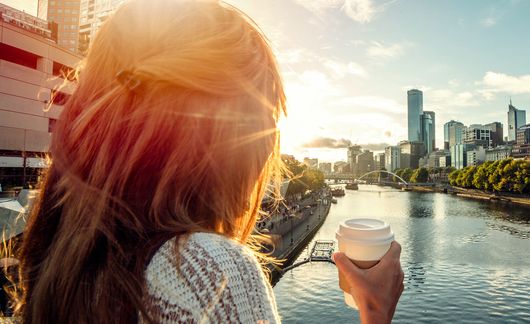 young woman drinking coffee on a bridge over a river in melbourne