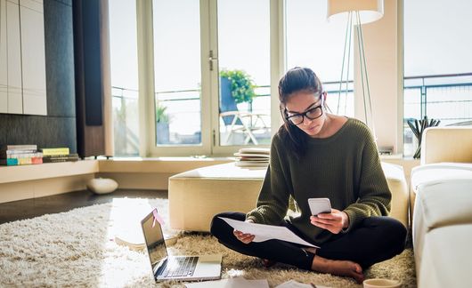 Young woman on her phone with her laptop out before her