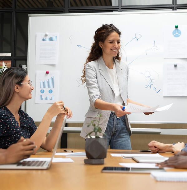 Female finance intern presenting to coworkers at a whiteboard in a conference room