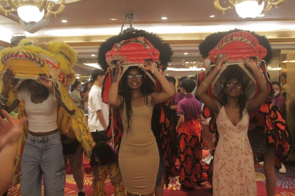 Three CIEE Global Navigator Students learn dragon dancing; they uphold two red and one yellow dragon heads. 