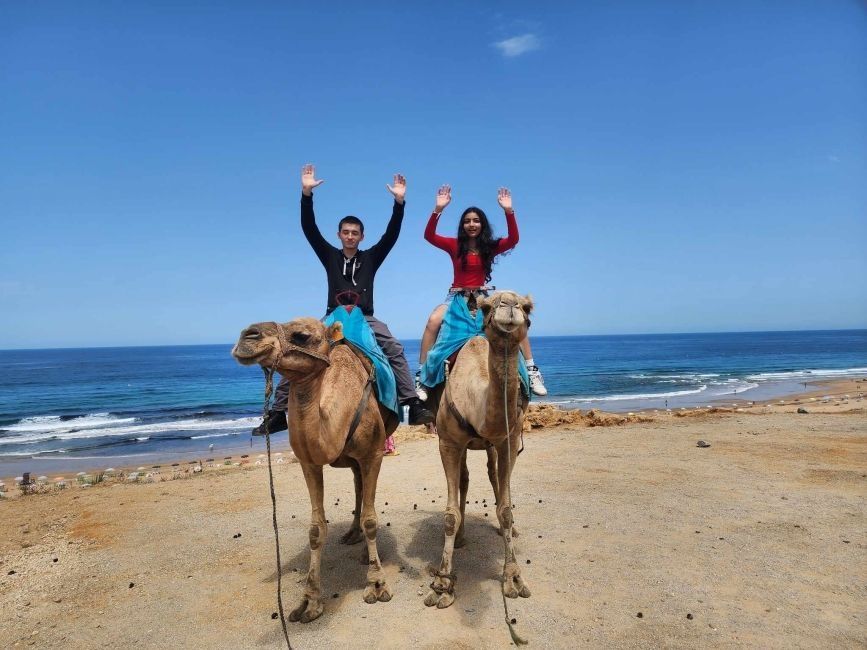 Two CIEE students sitting on camels with their arms raised