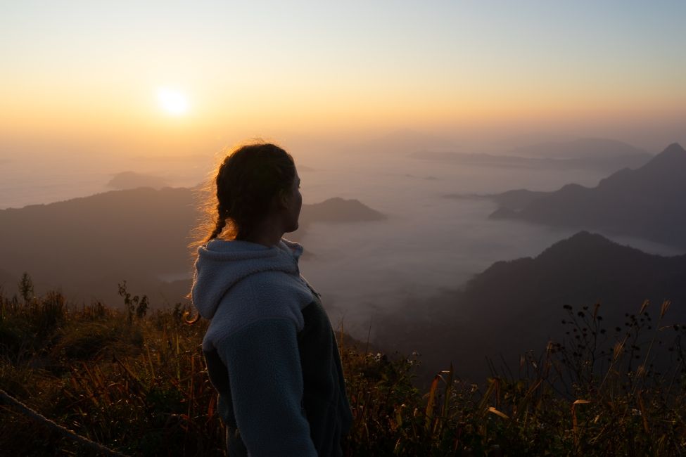 Girl looking out onto a view of fog and sunrise. 