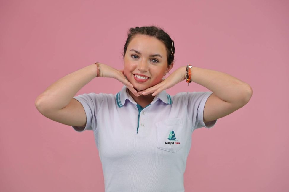A girl in a white polo poses in front of a pink background