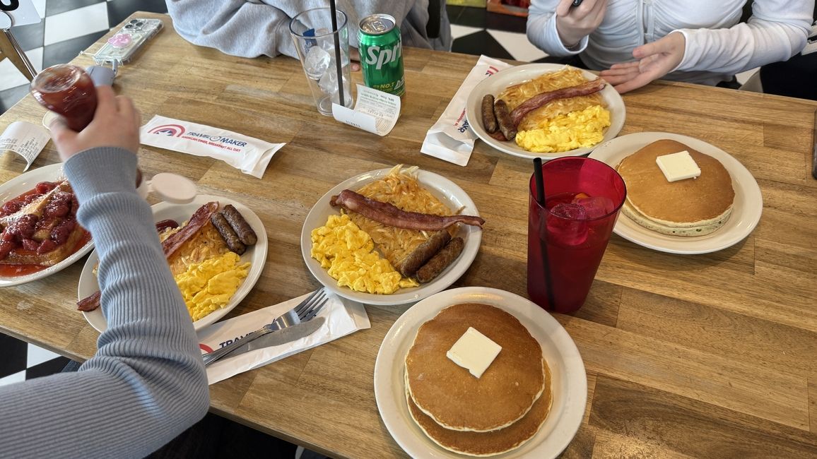 a table with an american style breakfast plating including pancakes, bacon, eggs, and hashbrowns