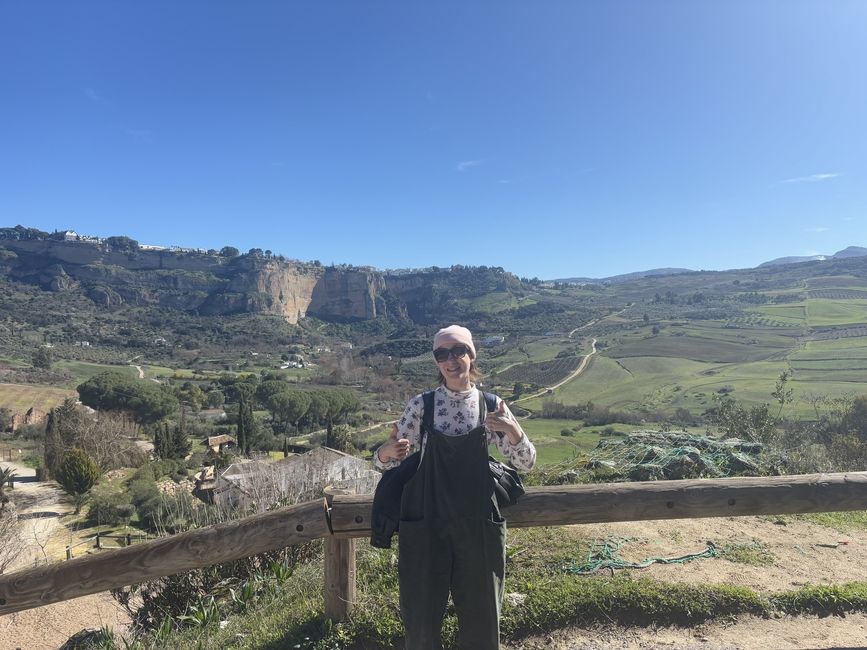 A girl in overalls standing in front of a dropoff that overlooks a rural valley in Ronda, Spain