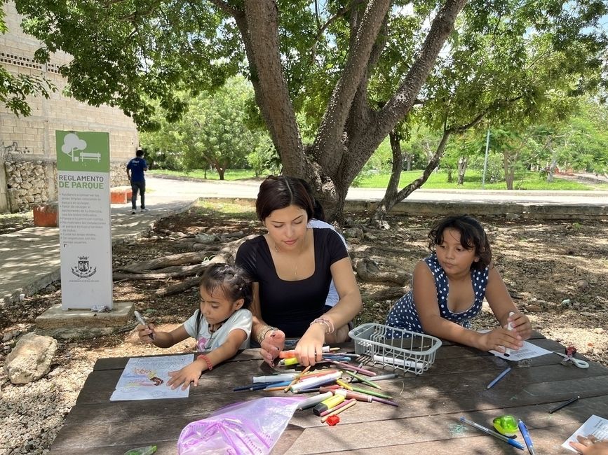 A student sits at a table and helps children draw while volunteering abroad