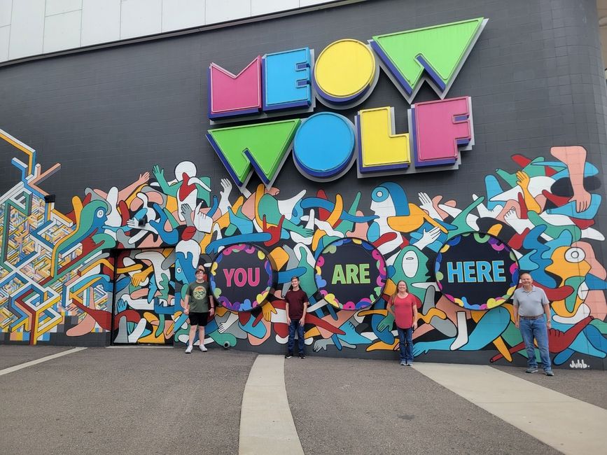 A Family Stands in Front of a sign for Denver's "Meow Wolf"