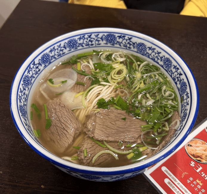 A bowl of warm pho with bean sprouts, cilantro, and beef.