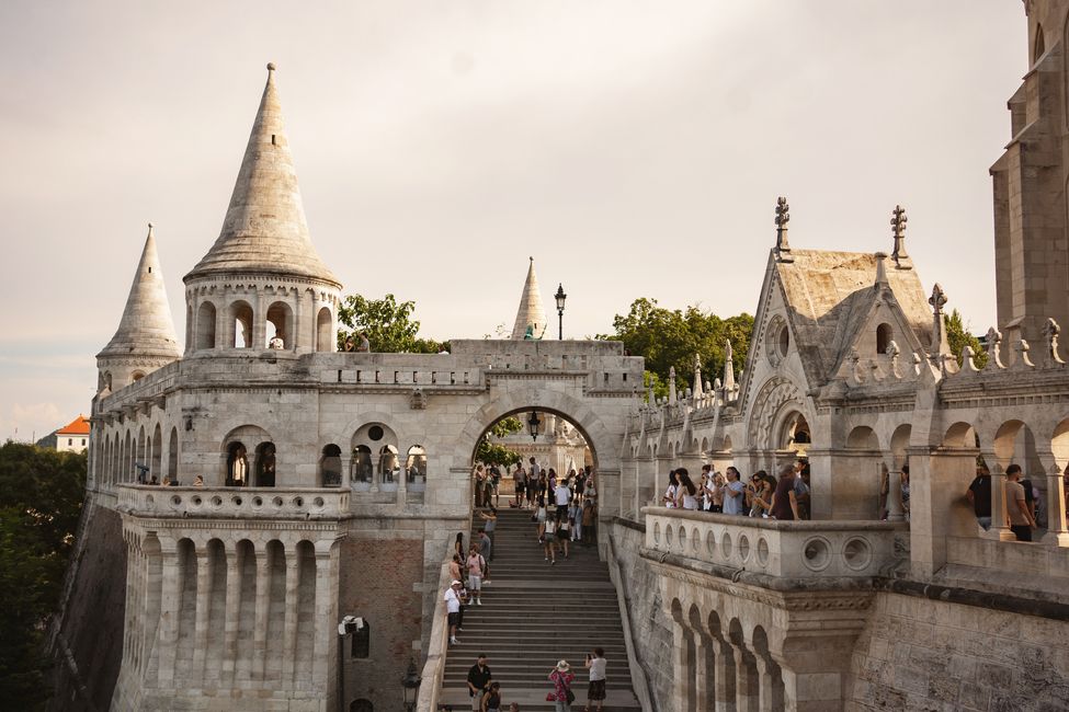 Tourists stroll through the elaborate Fisherman's Bastion in Budapest, admiring the unique towers and enjoying the beautiful evening light.