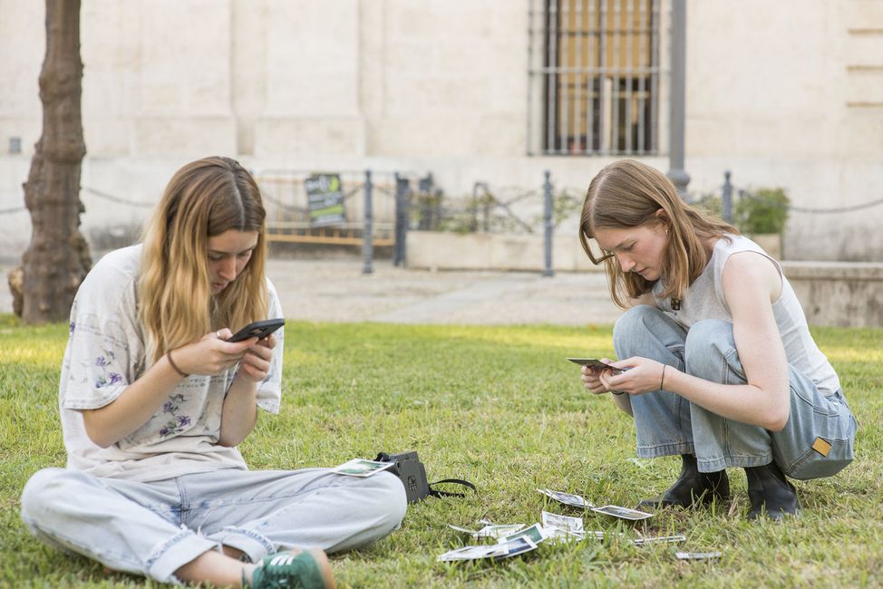high schoolers on their phones outside in the grass