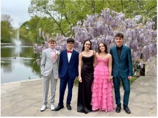 A group of five students in tuxedos and prom dresses posing in front of a lake