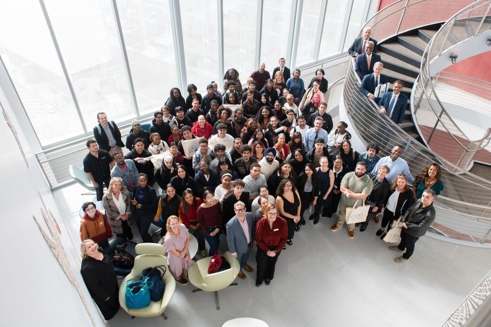 A group of roughly 50 people (BMCC students and staff and CIEE staff) standing in a room and smiling up into the photo captured from above