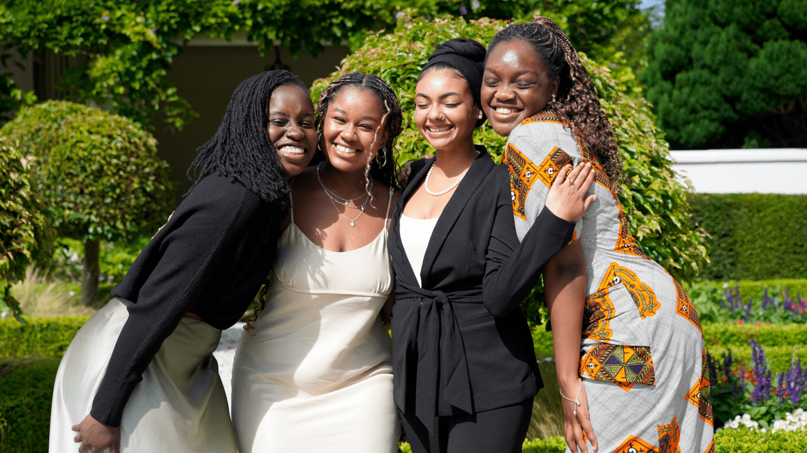 Four female students smiling cheek-to-cheek in front of a green, garden background