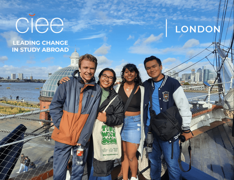 Four students stand together on a ship deck in London, smiling at the camera with the Thames River and city skyline behind them. A glass-domed building and cables from the ship frame the background, with a CIEE logo and the words “Leading Change in Study Abroad | London” visible in the corner.