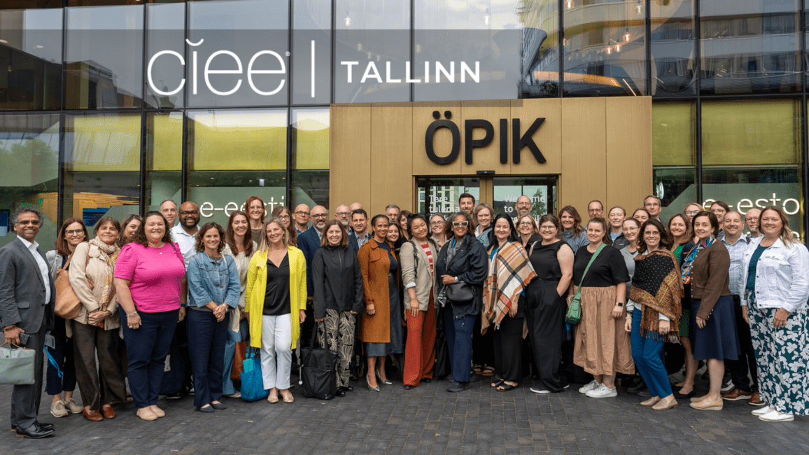 A group of 21 people stand together smiling out front of a newer looking building with "OPIK" as a logo on the building. Top left is "CIEE Tallinn" label.