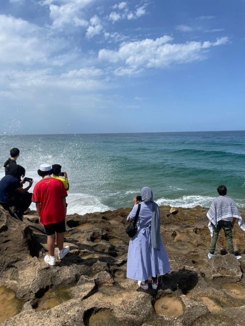 Students standing on a rock in front of crashing waves, looking out over the water