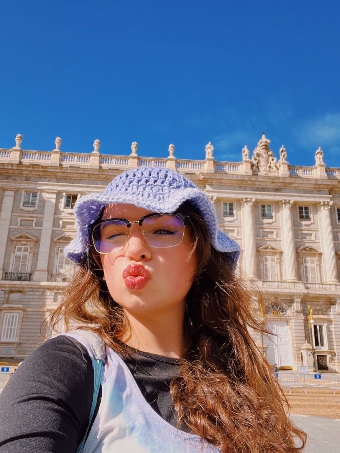 A young woman in a purple hat posing in front of the Royal Palace in Madrid, Spain
