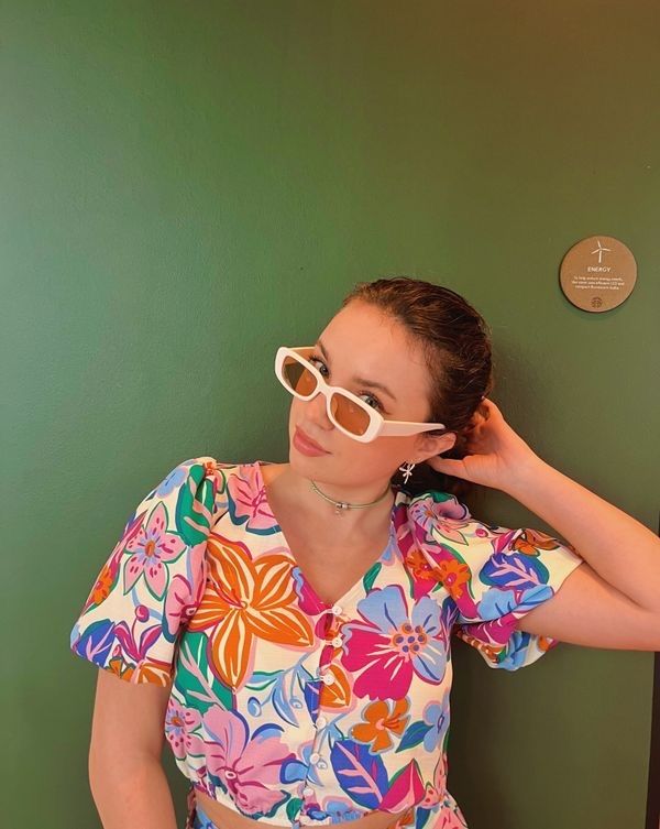 A girl in a colorful shirt and sunglasses against a green backdrop