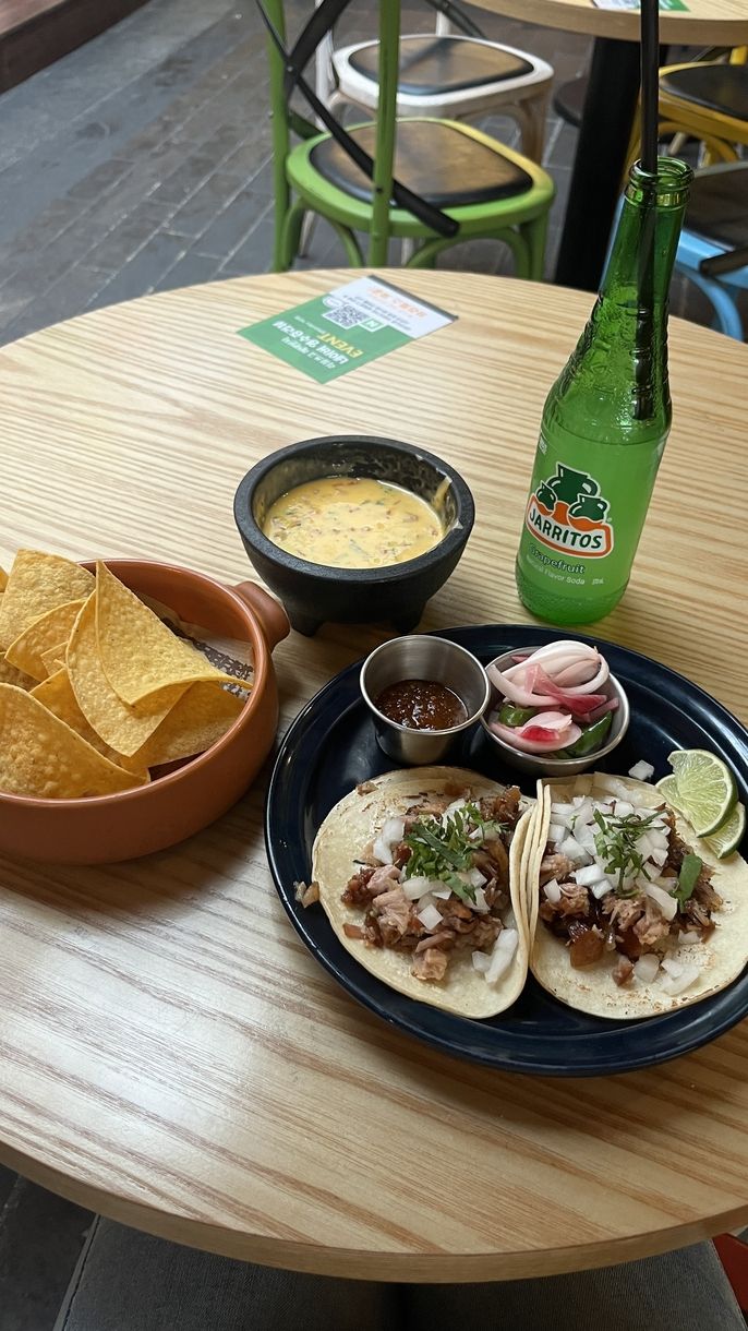 a picture of two carnitas tacos with a side of chips and a bowl of queso