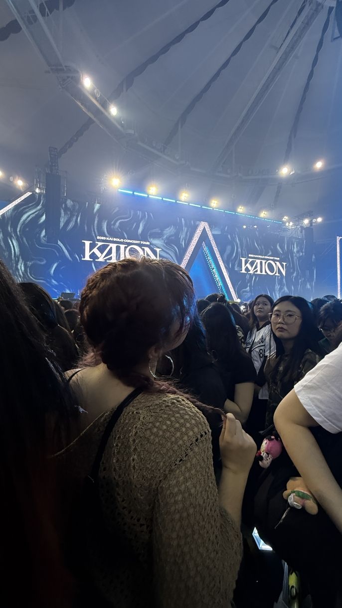 A girl is standing in the crowd of a concert facing the stage, away from the camera