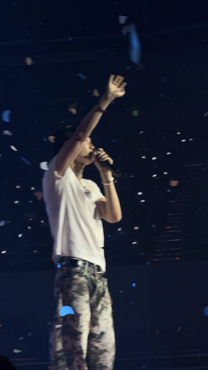 Kpop artist Kai is standing on stage waving to his fans as confetti falls around him