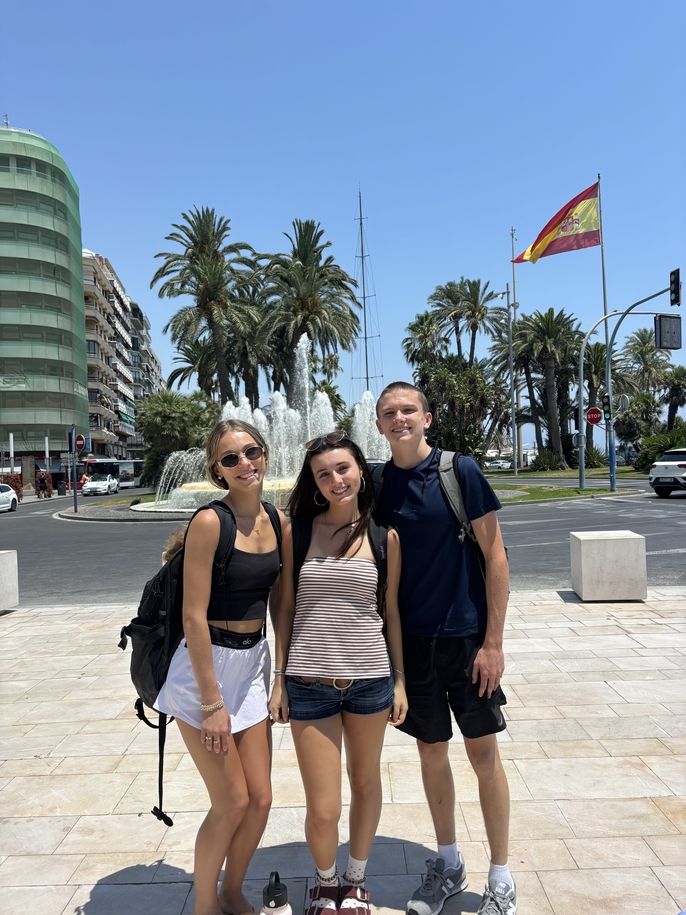 Students stand in front of the Spanish flag and a beautiful fountain and their first tour of the city.