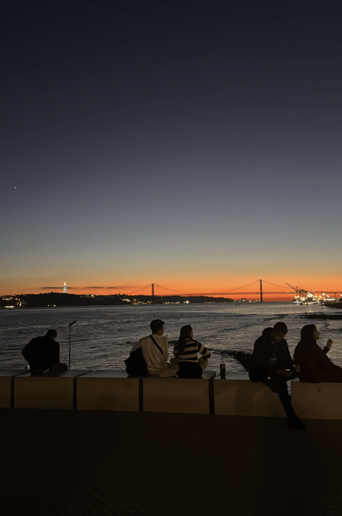 Cais do Sodré sunset, people sitting and talking by the river. 