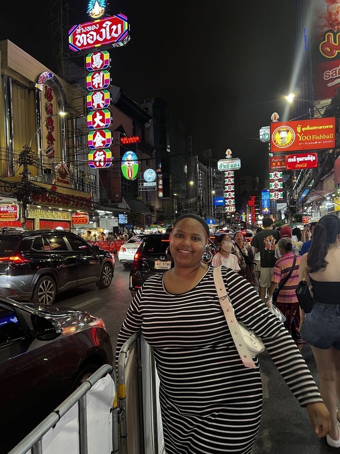Ciani wears a black and white striped dress and poses in front of a neon sign in bangkok china town