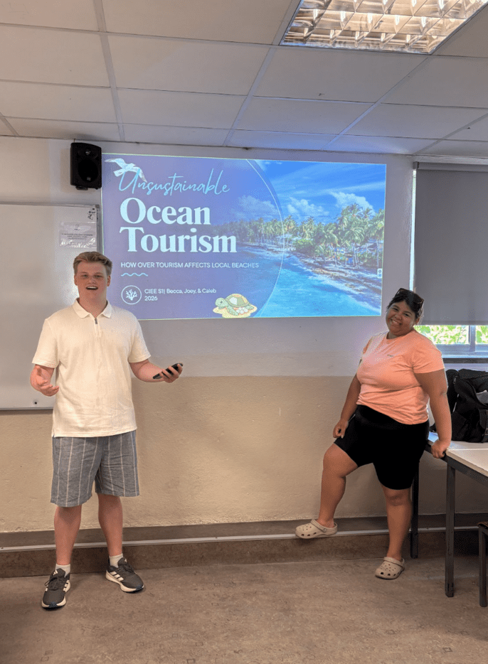 Two students present on the impacts of ocean tourism in front of a classroom presentation titled "Unsustainable Ocean Tourism."