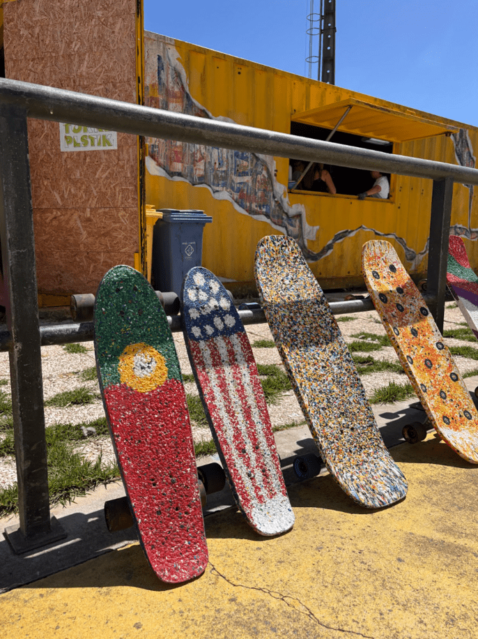 Colorful skateboards made from recycled plastic are displayed outside a workshop on a sunny day.