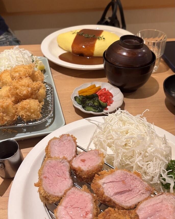 A white plate with a giant egg omlet sitting on top of rice and a second plate with cut up pork.