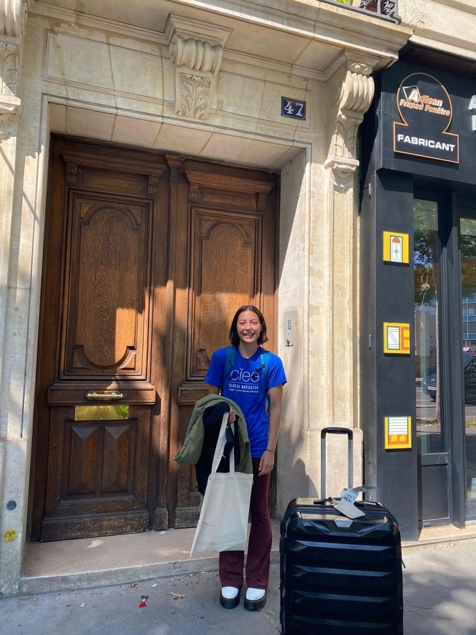 Global Navigator student standing in front of giant door with suitcase