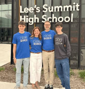 two male students and their host parents wearing with blue shirts with the ciee logo and standing in front of a "lee's summit high school" sign 