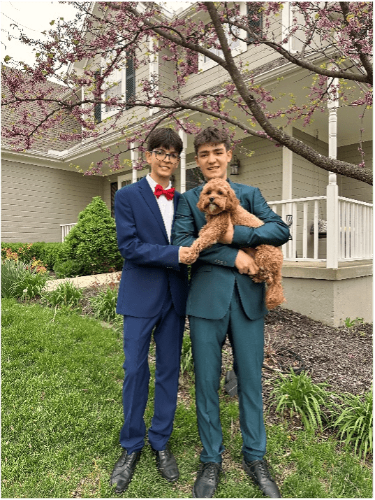 two male students dressed in formal suits holding a brown dog in front of a house - they are heading to prom