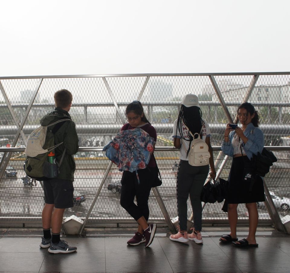 The students stand on a sky-bridge while it rains