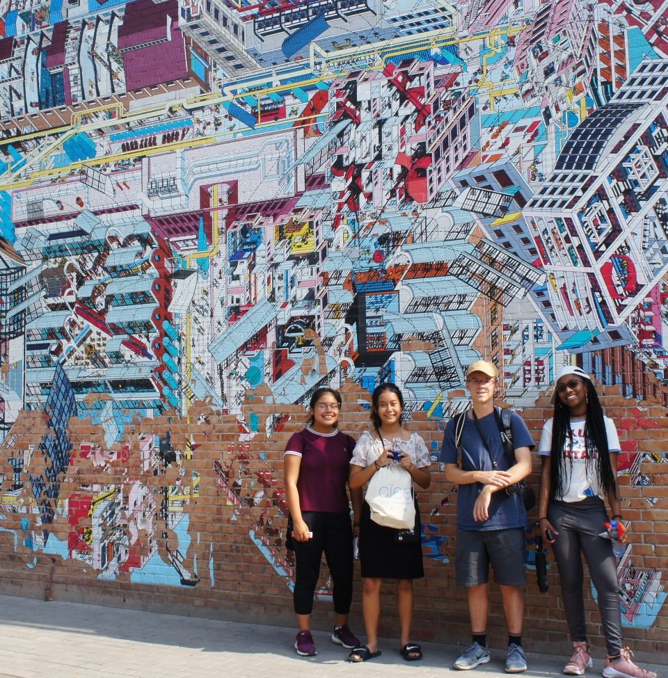 The students stand in front of a mural