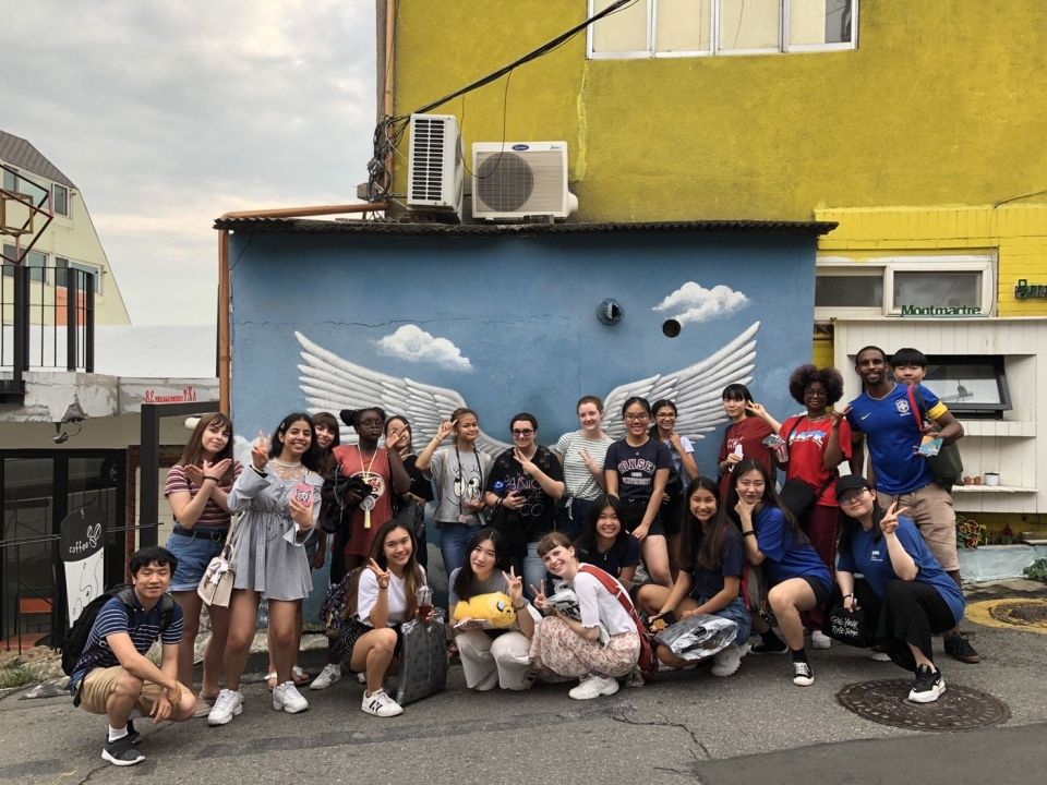 Group picture of students and leaders in front of a mural of angel's wings.