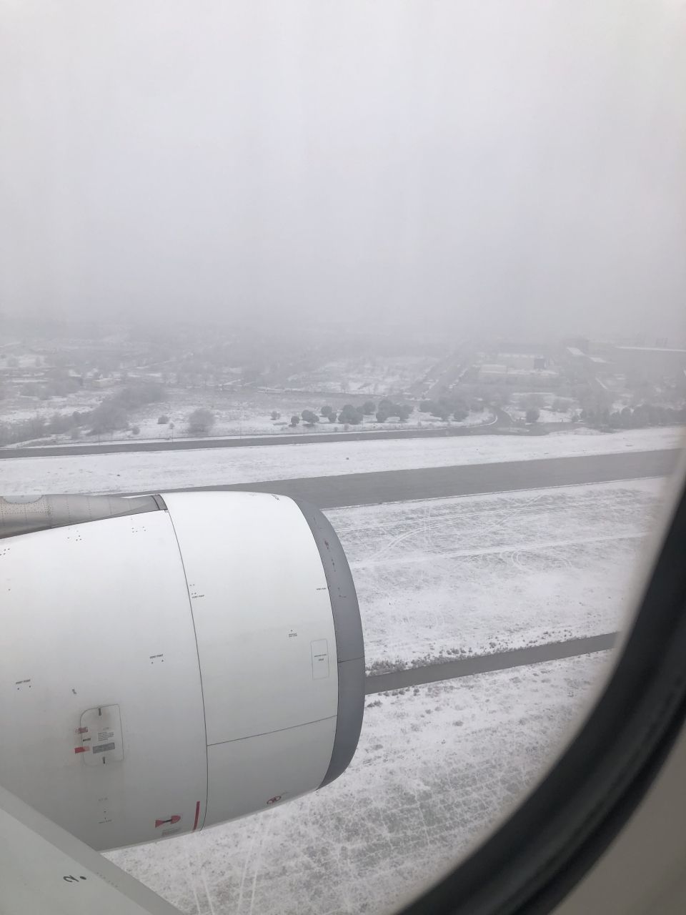 Looking outside an airplane window at an engine and a very snowy runway/town.