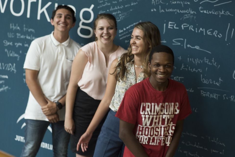 A diverse group of four CIEE global internship students, both male and female, smiling in front of a chalk board. 