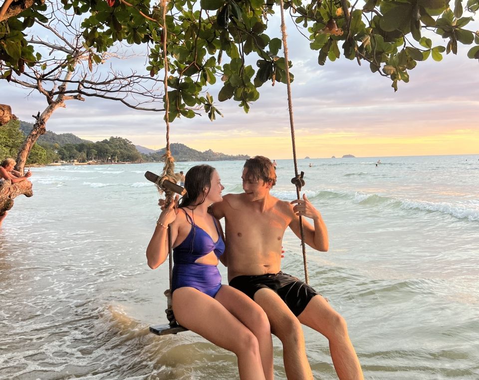 Two people sitting on a beach swing with a sunset in the background. 