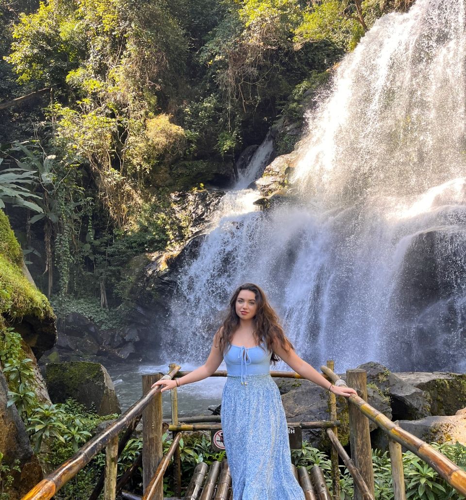 a young woman in a blue outfit poses in front of a waterfall