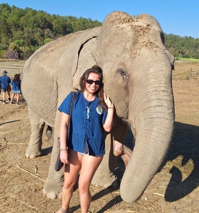 Young woman in a blue button shirt and sunglasses poses with an elepant