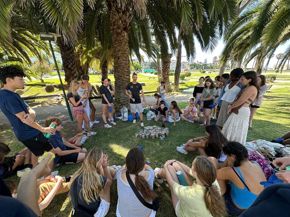 Students sit in a circle on the grass around plastic cups filled with with cigarette butts.