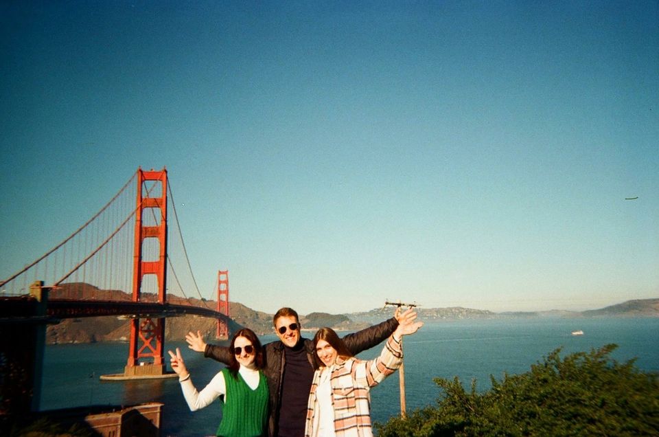 Three people posing with their arms up in front of the Golden Gate Bridge
