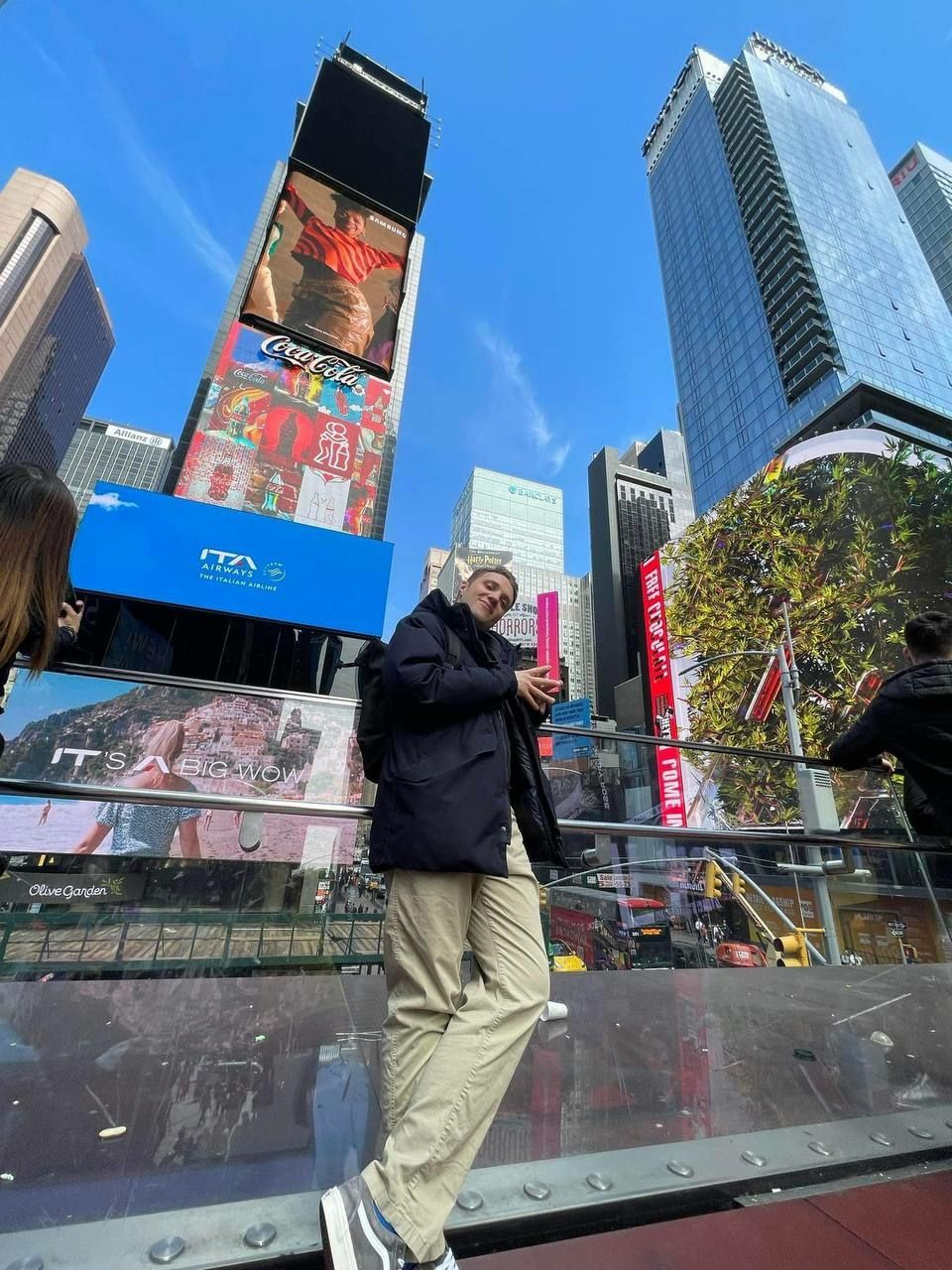 A mid-20s age man smiling and standing in front of billboards in Time Square New York