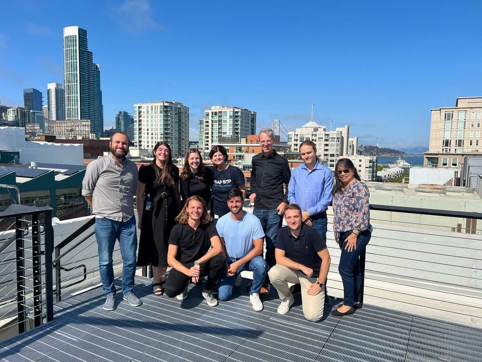 Ten people standing on a balcony smiling together in front of the San Franciso skyline