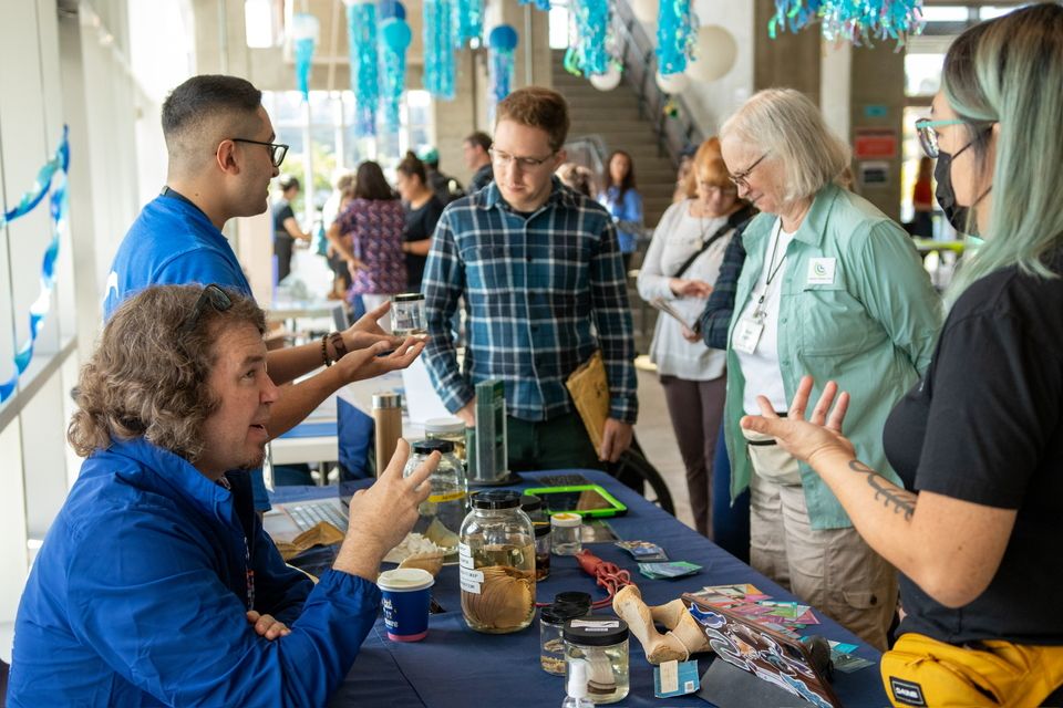 A table of people in blue discussing sea conservation with three guests, all middle aged