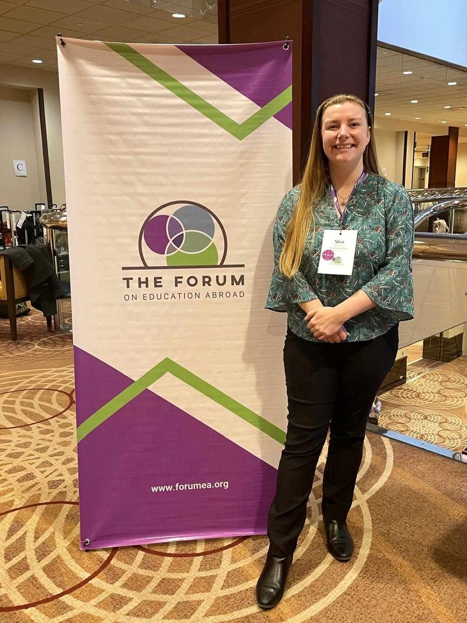 A professional standing in front of a sign that says "The Forum on Education Abroad"